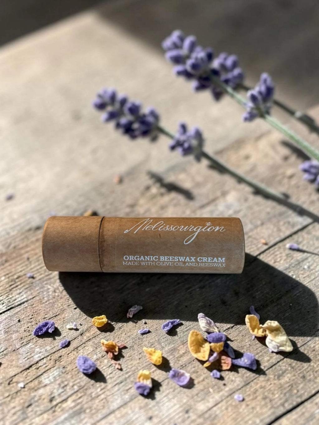 Bio-Bienenwachs-Repair-Balsam, beiger Stick in Papierhülle, auf Holz mit Blüten