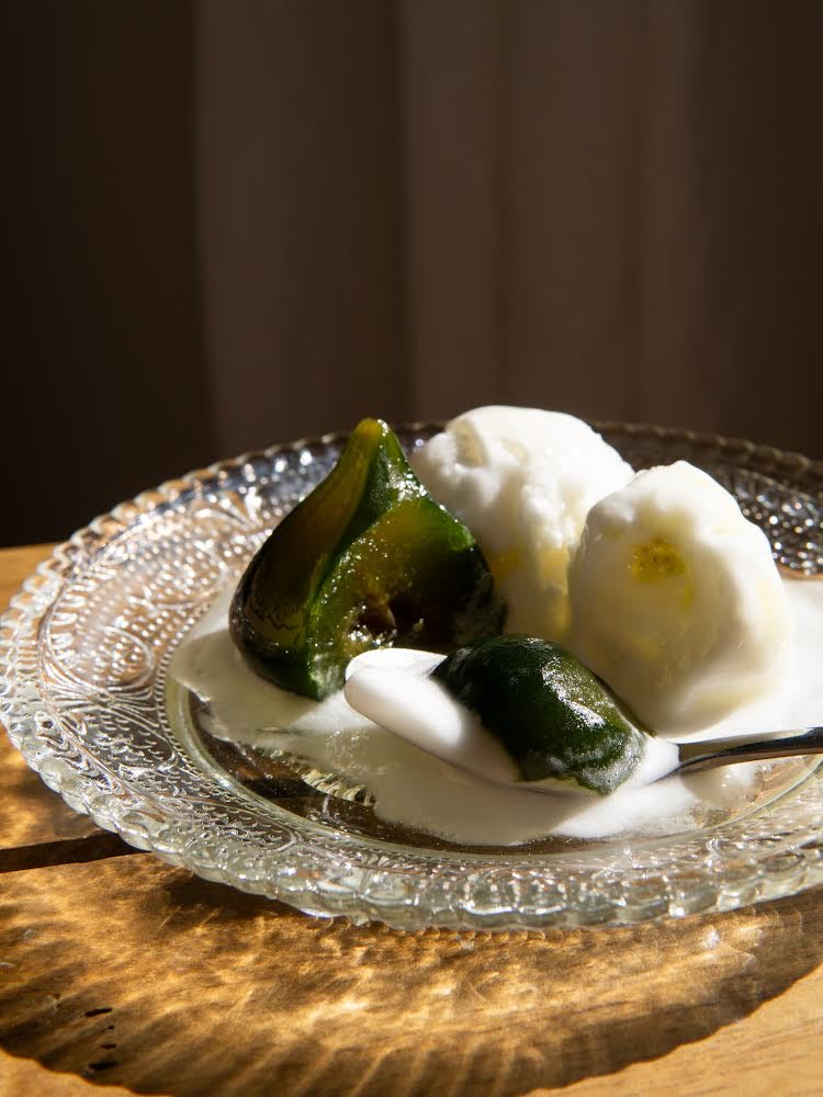 Dessertteller mit grünen Feigenstücken und weißer Sahne auf Glasplatte